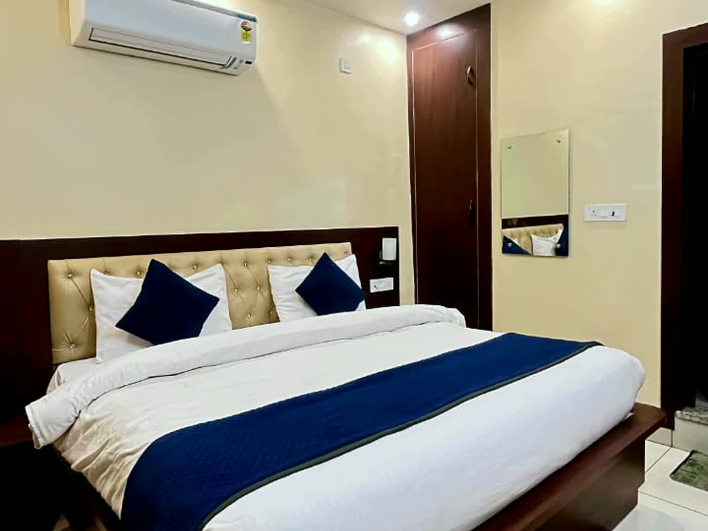A guest room with a padded headboard, navy runner and an air conditioning unit above the bed.